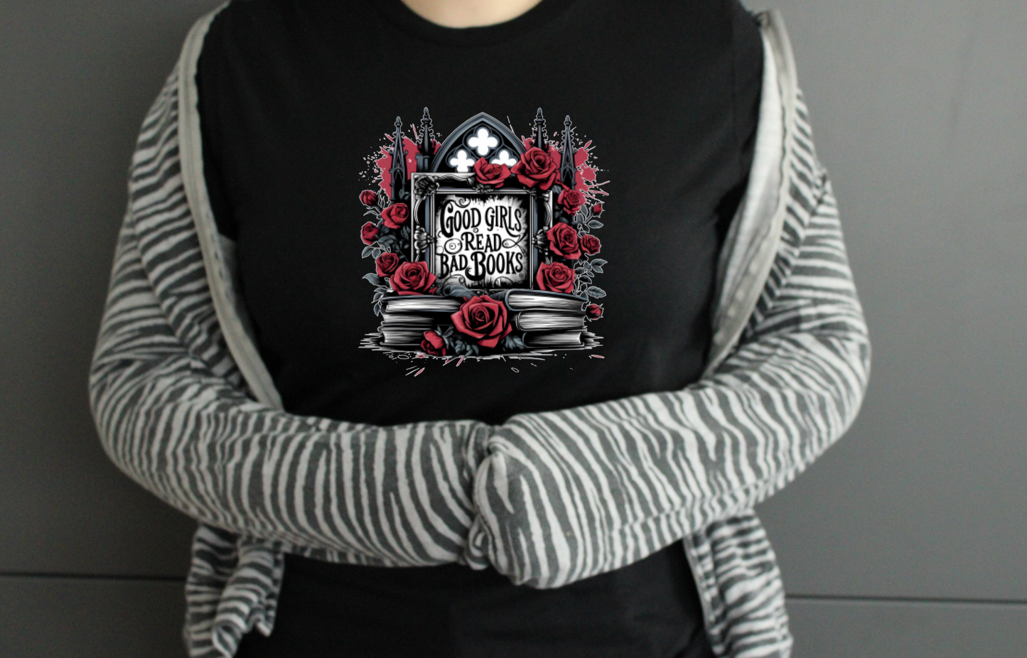 Person wearing a black tshirt with a graphic design saying Good Girls Read Bad Books ideal for BookTok or Book Lovers, on a grey background