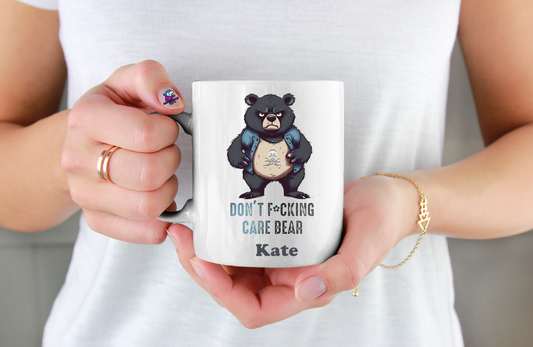 Person holding a mug with a graphic design of a bear and text, wearing a white shirt.