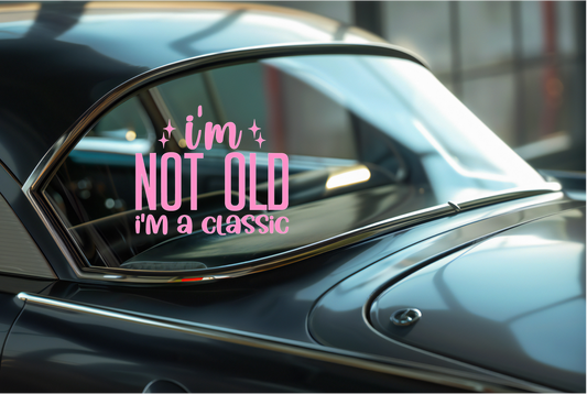 Car window sticker with a pink decal reading 'i'm not old i'm a classic' on a blurred background