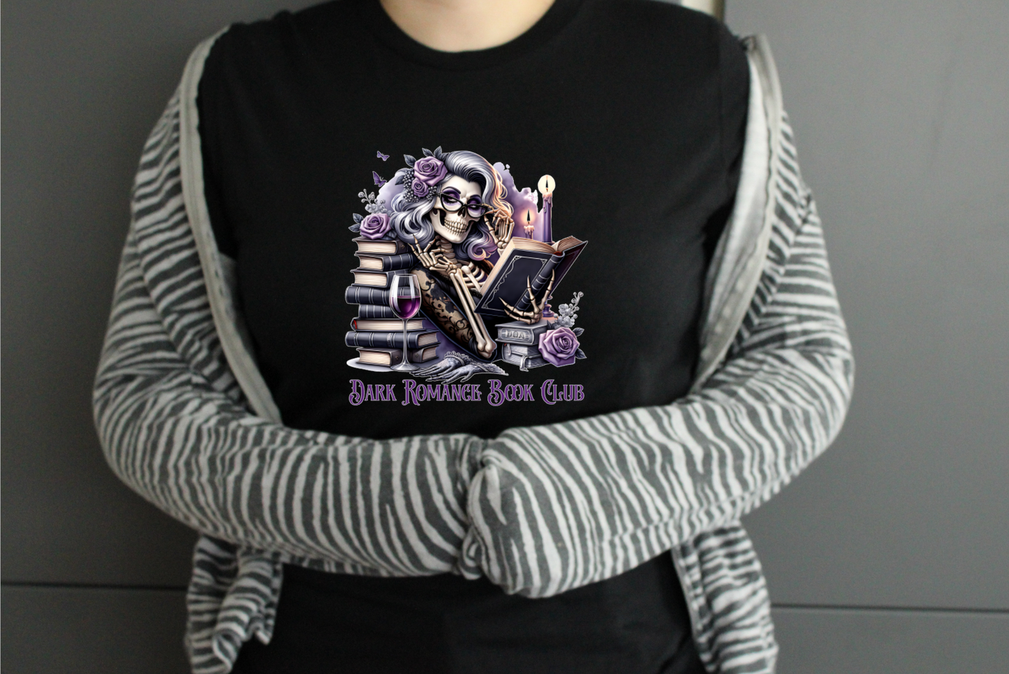 Person wearing a black tshirt with a graphic design and text saying Dark Romance Book Club, standing against a plain background.