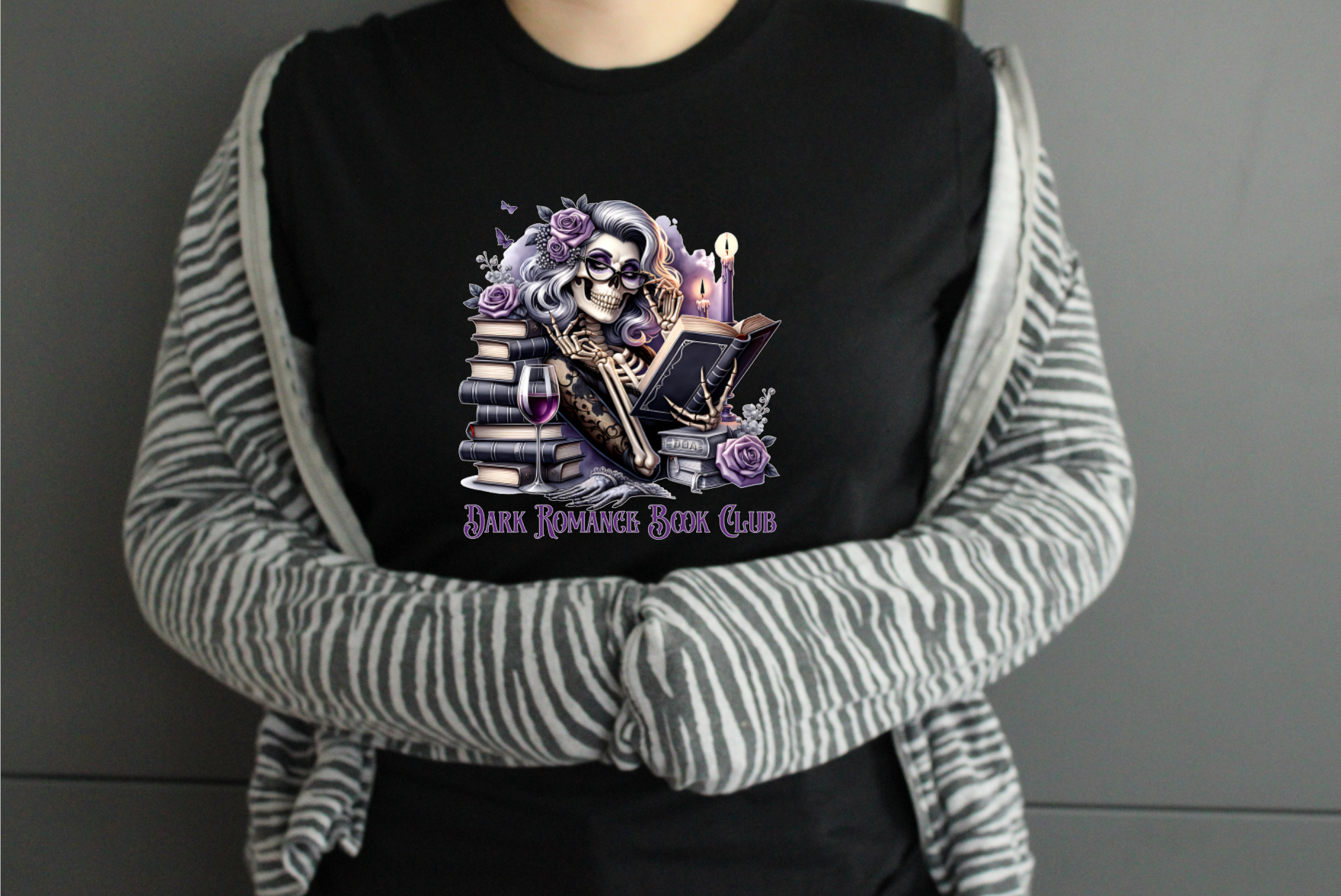 Person wearing a black tshirt with a graphic design and text saying Dark Romance Book Club, standing against a plain background.