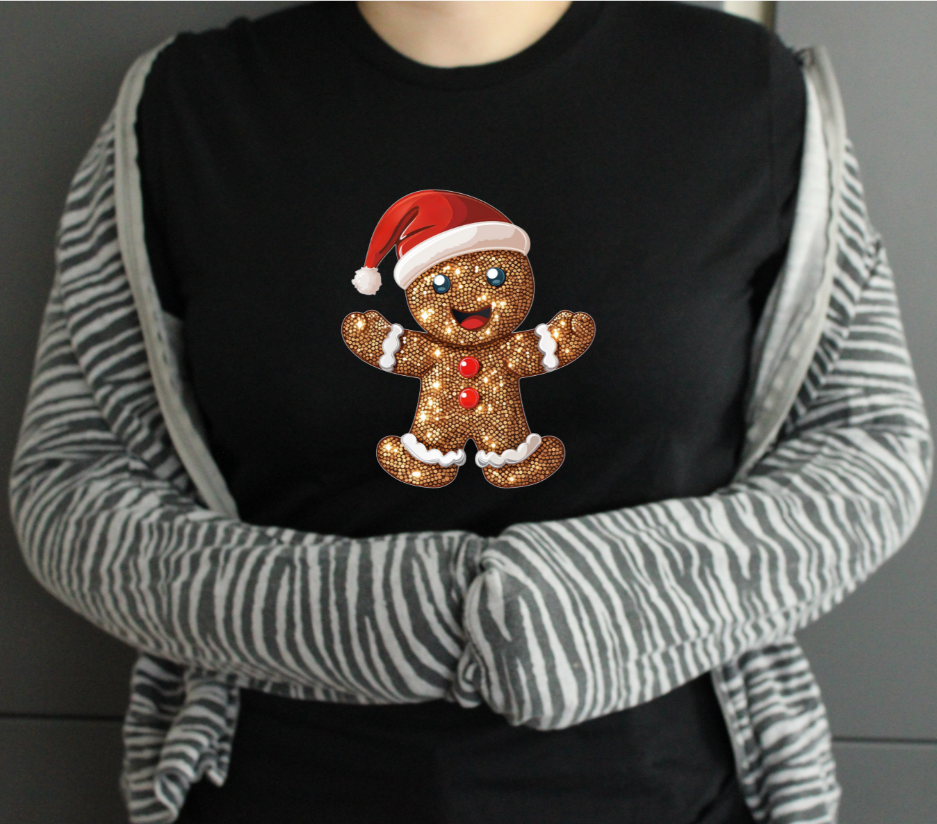 Person wearing a black tshirt with a glitter christmas gingerbread man design on a gray background