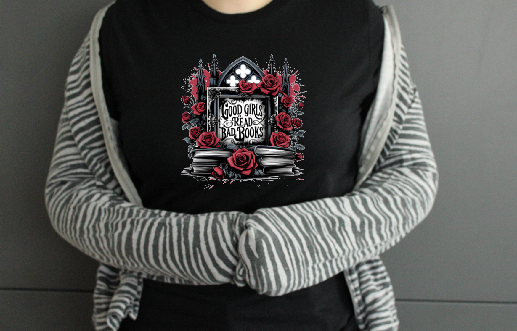 Person wearing a black tshirt with a graphic design saying Good Girls Read Bad Books ideal for BookTok or Book Lovers, on a grey background 