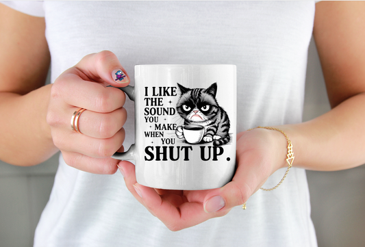 Person holding a mug with a cat graphic and text, wearing a white shirt.