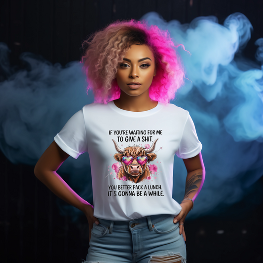 Person wearing a white t-shirt with a graphic Highland Cow and text, standing against a colourful smoke background.