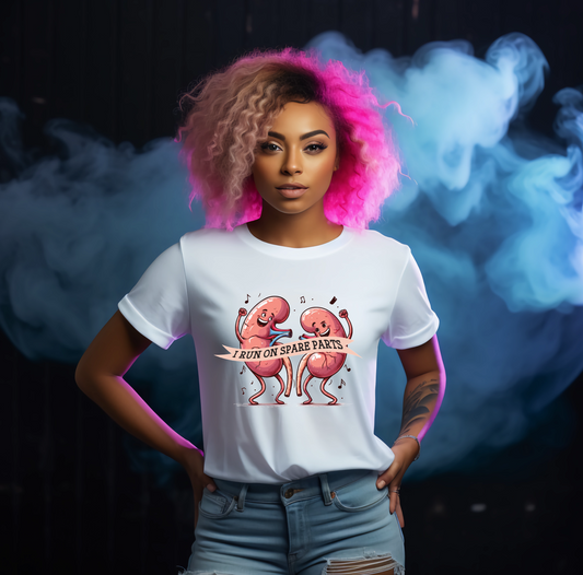 Person wearing a white t-shirt with a graphic design and text saying i run on spare parts for kidney transplant awareness, standing against a dark background with smoke effects.