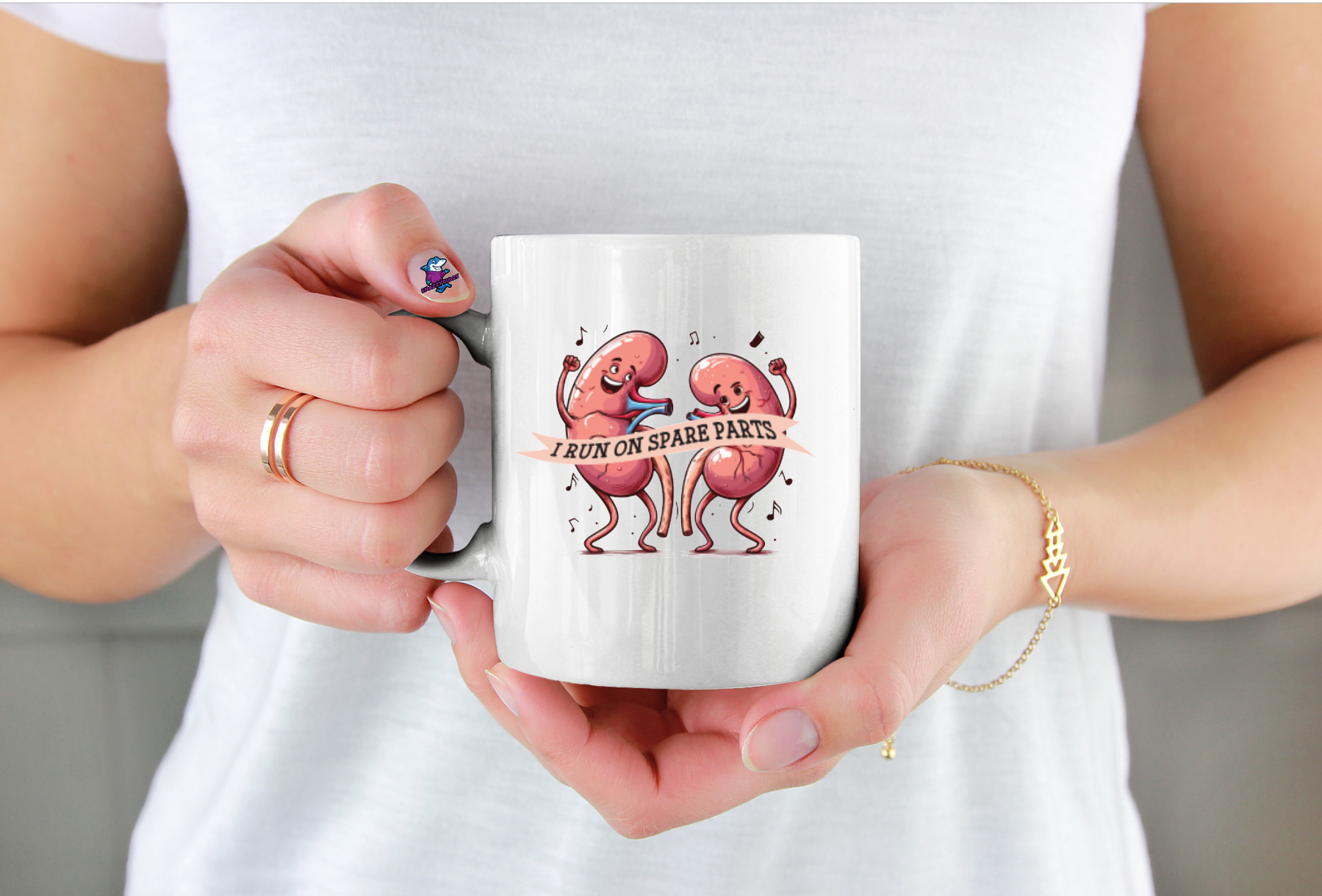 Person holding a white mug with cartoon characters and text saying I run on Spare Parts for kidney awareness