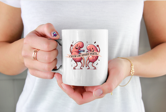 Person holding a white mug with cartoon characters and text saying I run on Spare Parts for kidney awareness