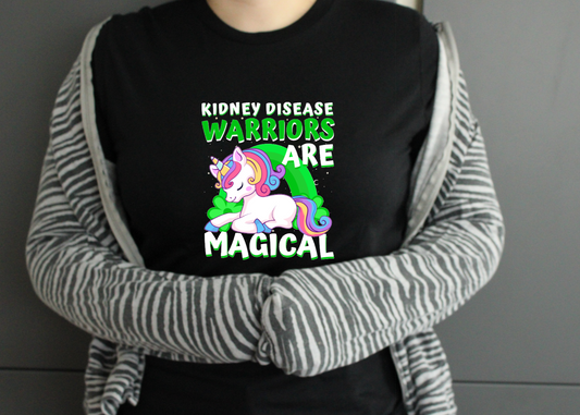 Person wearing a black shirt with a unicorn graphic and text, standing against a neutral background kidney disease warriors are magical text