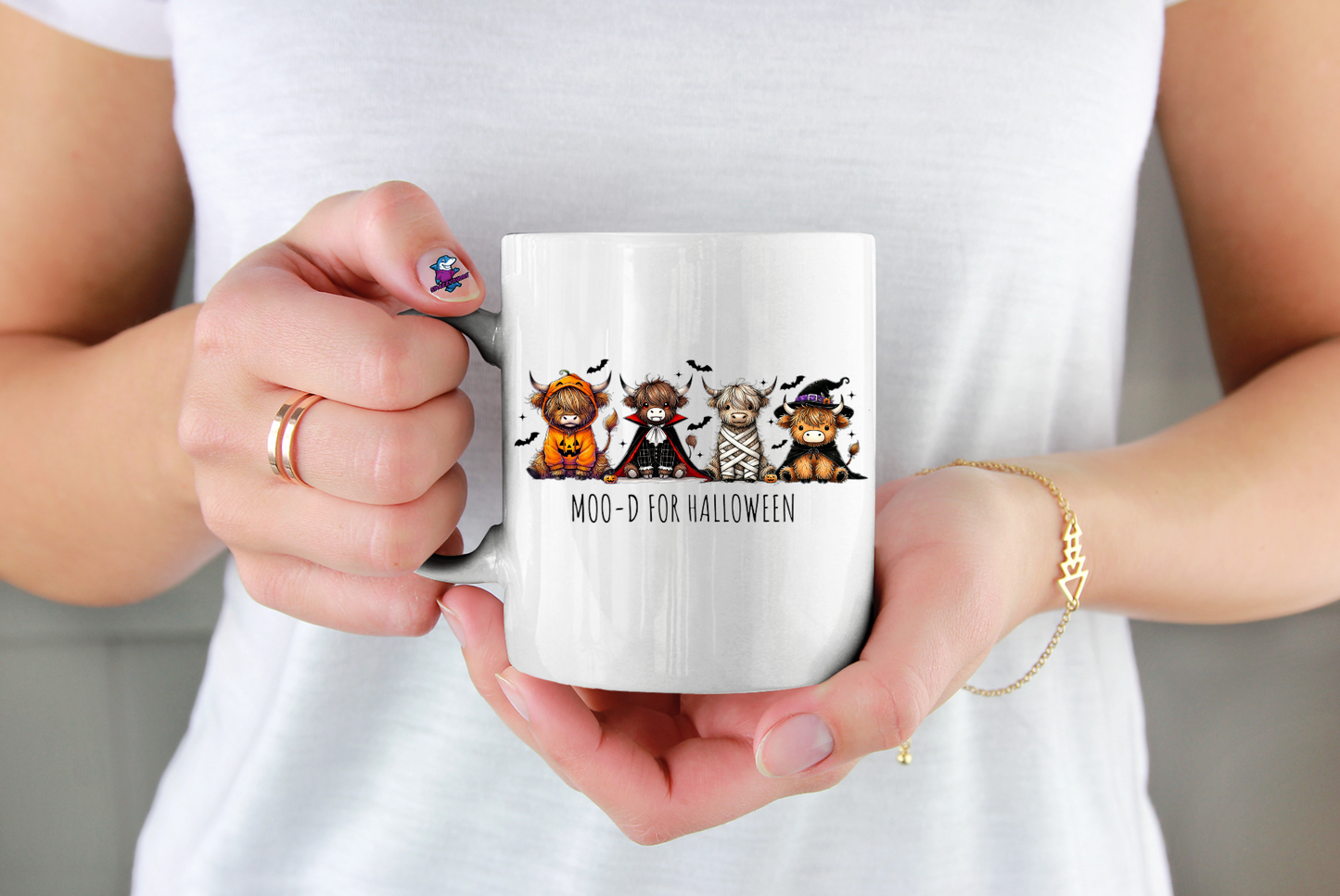 Person holding a white mug with Halloween-themed design featuring cartoon cows in costumes.