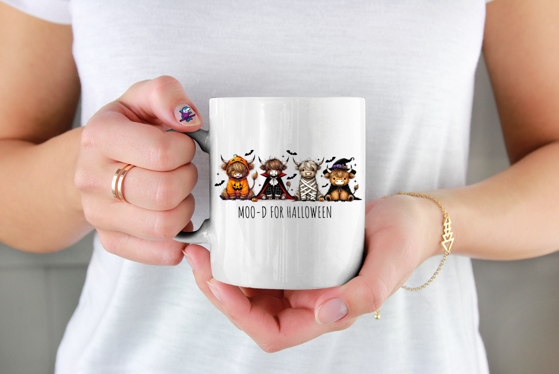 Person holding a white mug with Halloween-themed design featuring cartoon cows in costumes.
