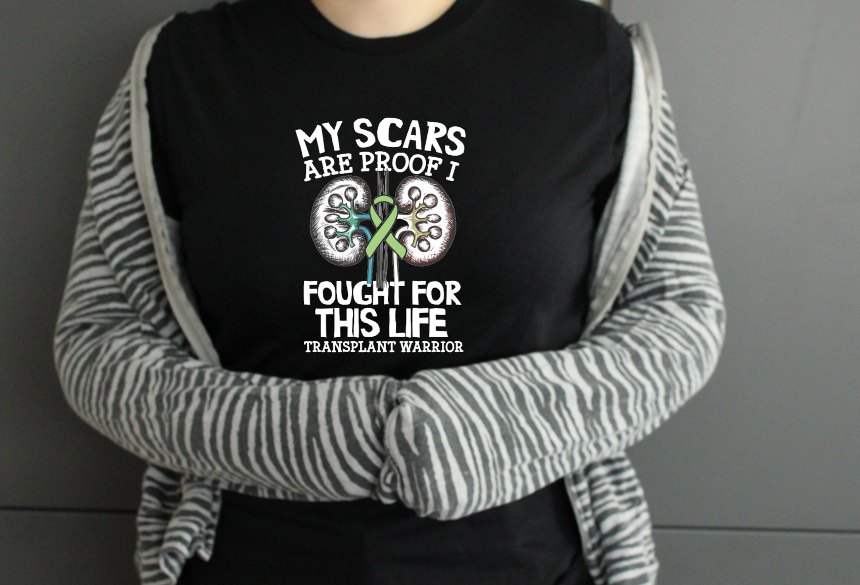 Person wearing a black t-shirt with a transplant warrior message and striped sleeves.