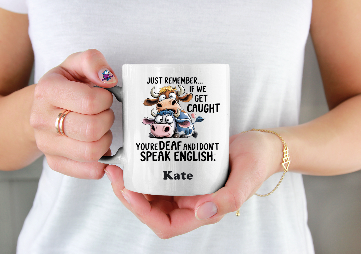 Person holding a mug with a cartoon cow and text, wearing a white shirt.