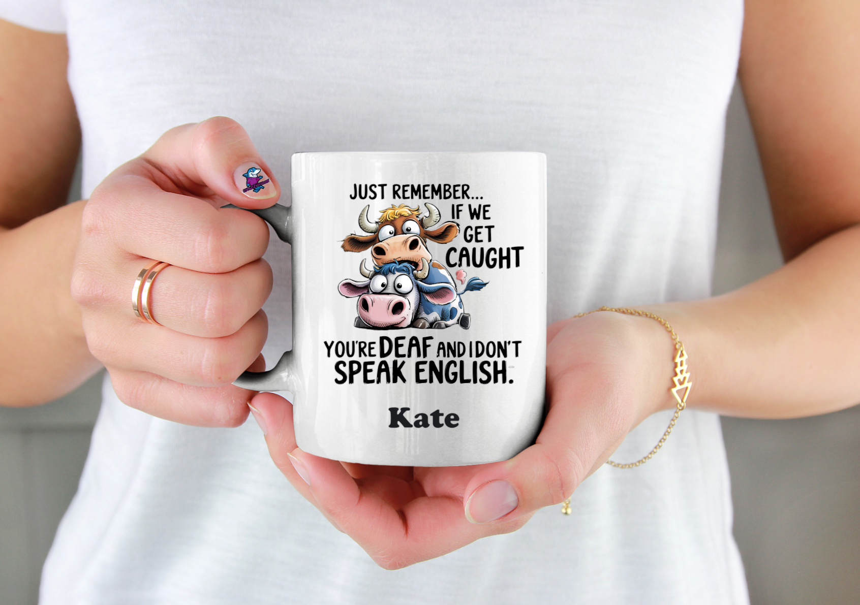 Person holding a mug with a cartoon cow and text, wearing a white shirt.
