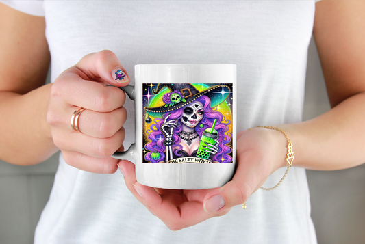 Person holding a mug with a colourful design featuring a skeleton and text saying The Salty Witch