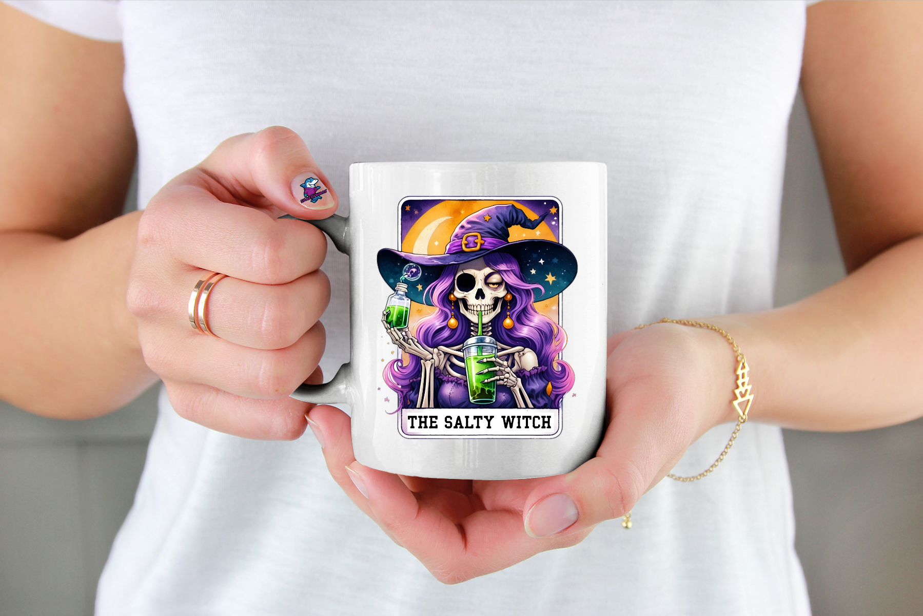 Person holding a mug with a skeleton witch design and 'The Salty Witch' text in a tarot card design image