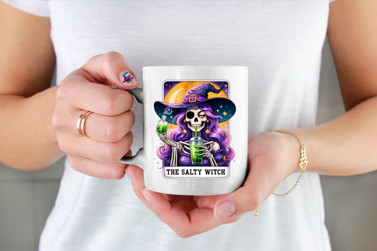 Person holding a mug with a skeleton witch design and 'The Salty Witch' text in a tarot card design image