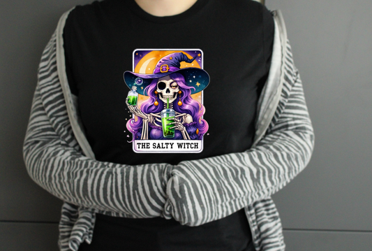 Person wearing a black t-shirt with a colourful graphic design of a tarot card witch and the text 'The Salty Witch'.