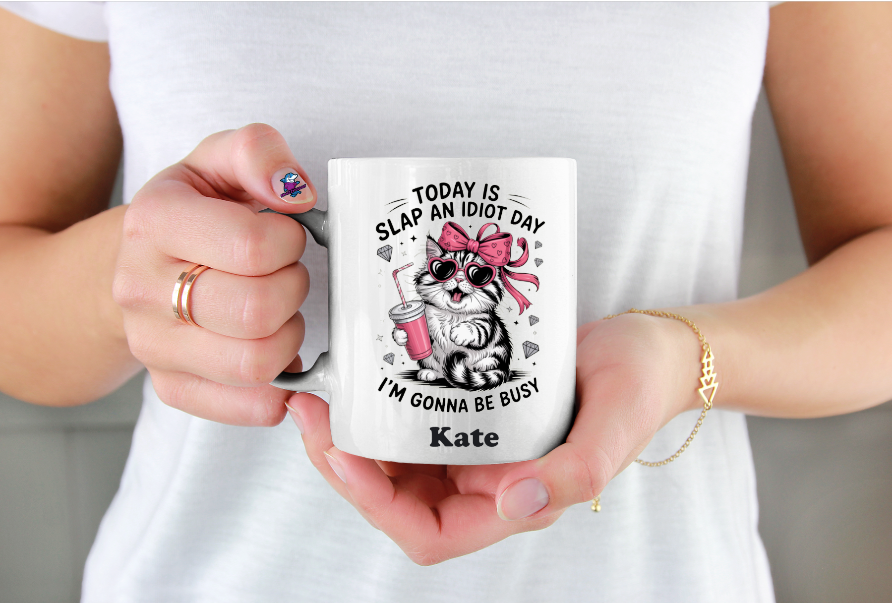 Person holding a mug with a cat graphic and text, wearing a white shirt.