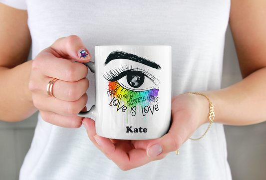 Person holding a mug with a colorful design and text, wearing a white shirt.