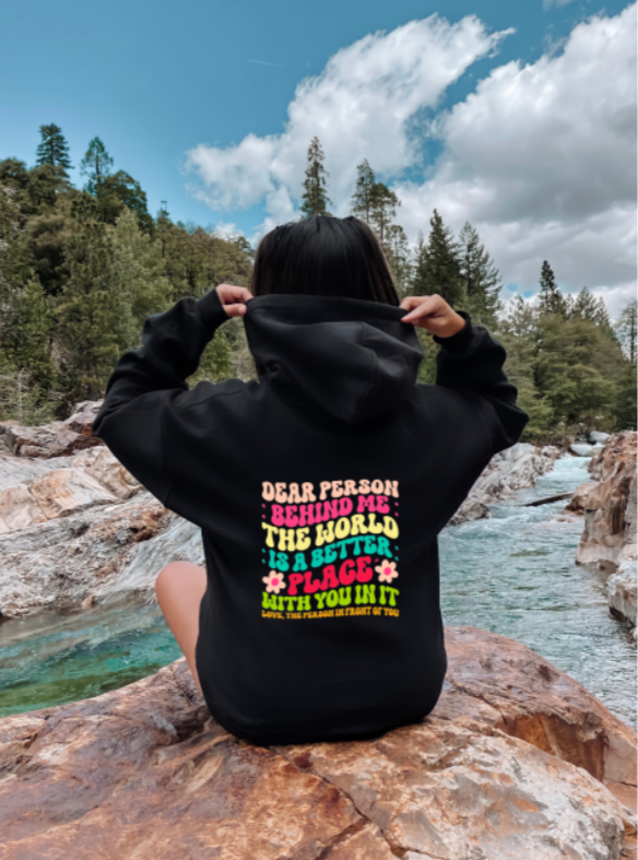 Person wearing a black hoodie with colorful text in a natural setting